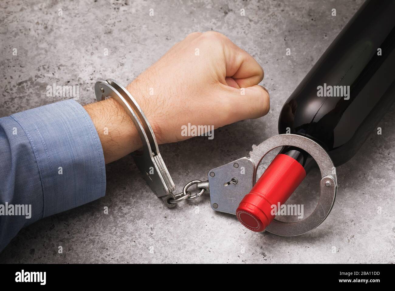 Die Hand ist mit Handschellen an die Flasche gefesselt. Das Konzept des Kampfes gegen Alkoholismus Stockfoto