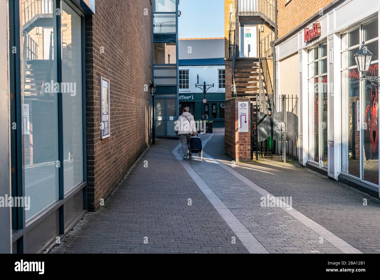 März 2020. Eine Frau geht am Nachmittag in der britischen Sperrstelle auf einer einsamen Gasse im Stadtzentrum entlang. Bicester, Oxfordshire, Großbritannien Stockfoto