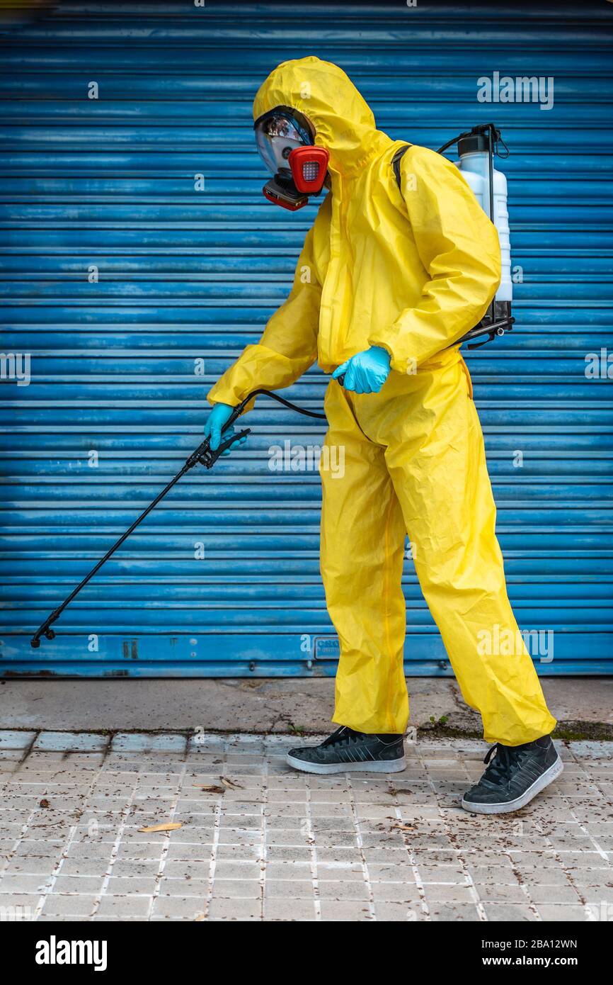Coronavirus. Ein Sanitärmitarbeiter, der eine Maske trägt und die Straßen mit alkoholbasierter Lösung unter Druck säubert. Desinfizieren gegen Corona. Stockfoto