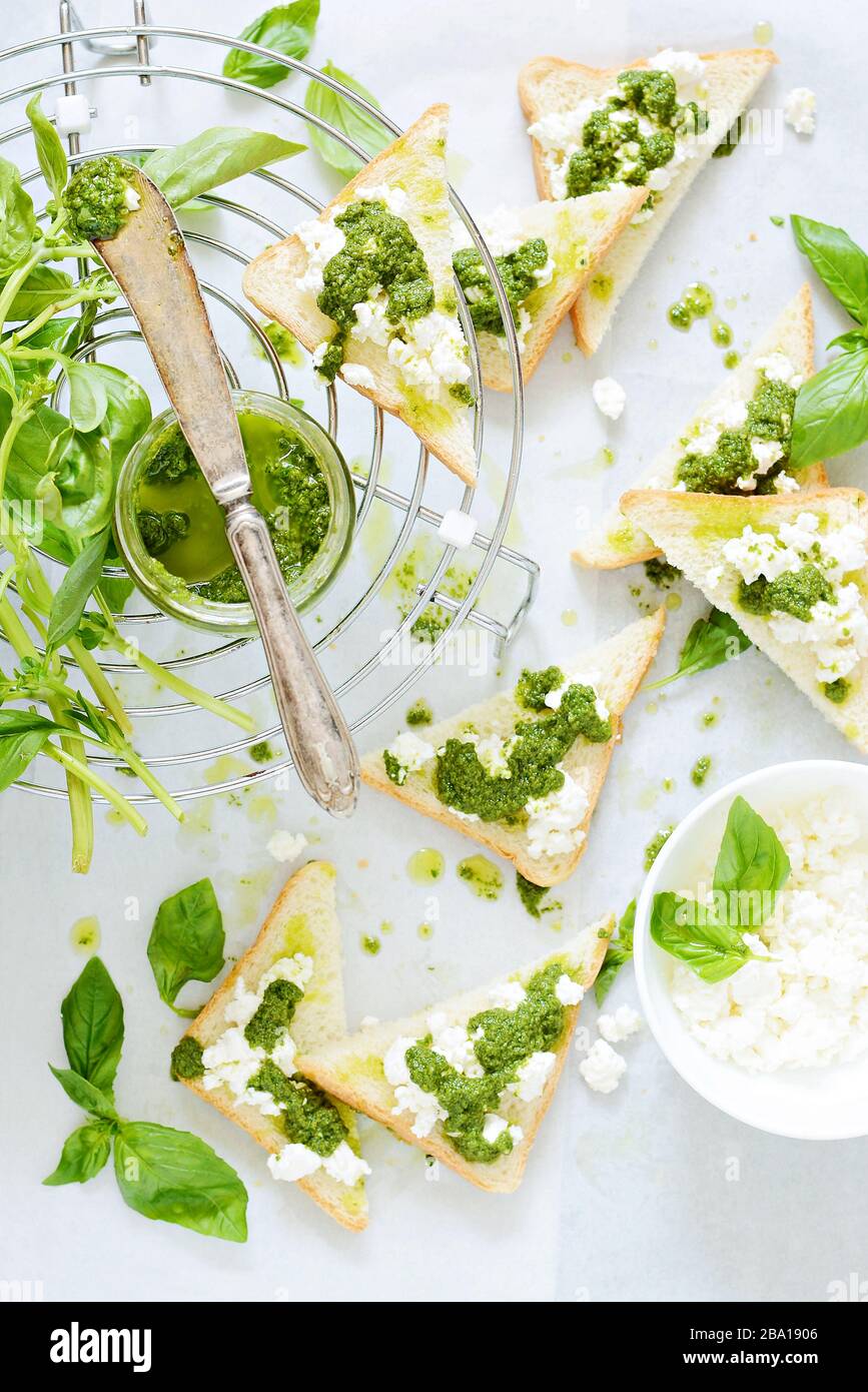 Knusprige Toast (Krostini, Bruschetta) mit Hüttenkäse (Ricotta) und frisch zubereitetem Pesto. Hausgemachte Basilika-Pechto-Soße in einem Glas auf einem hellen Backgroschen Stockfoto