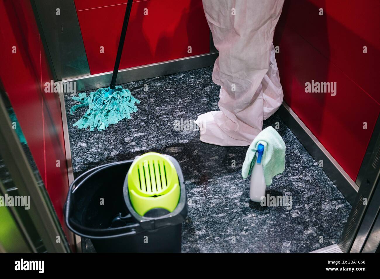 Eine Person, die eine Maske, Handschuhe und einen Sicherheitsanzug trägt, reinigt und desinfiziert eine Tür einer Gemeinschaftswohnung angesichts einer Virus-Pandemie, einer geschützten Safette Stockfoto