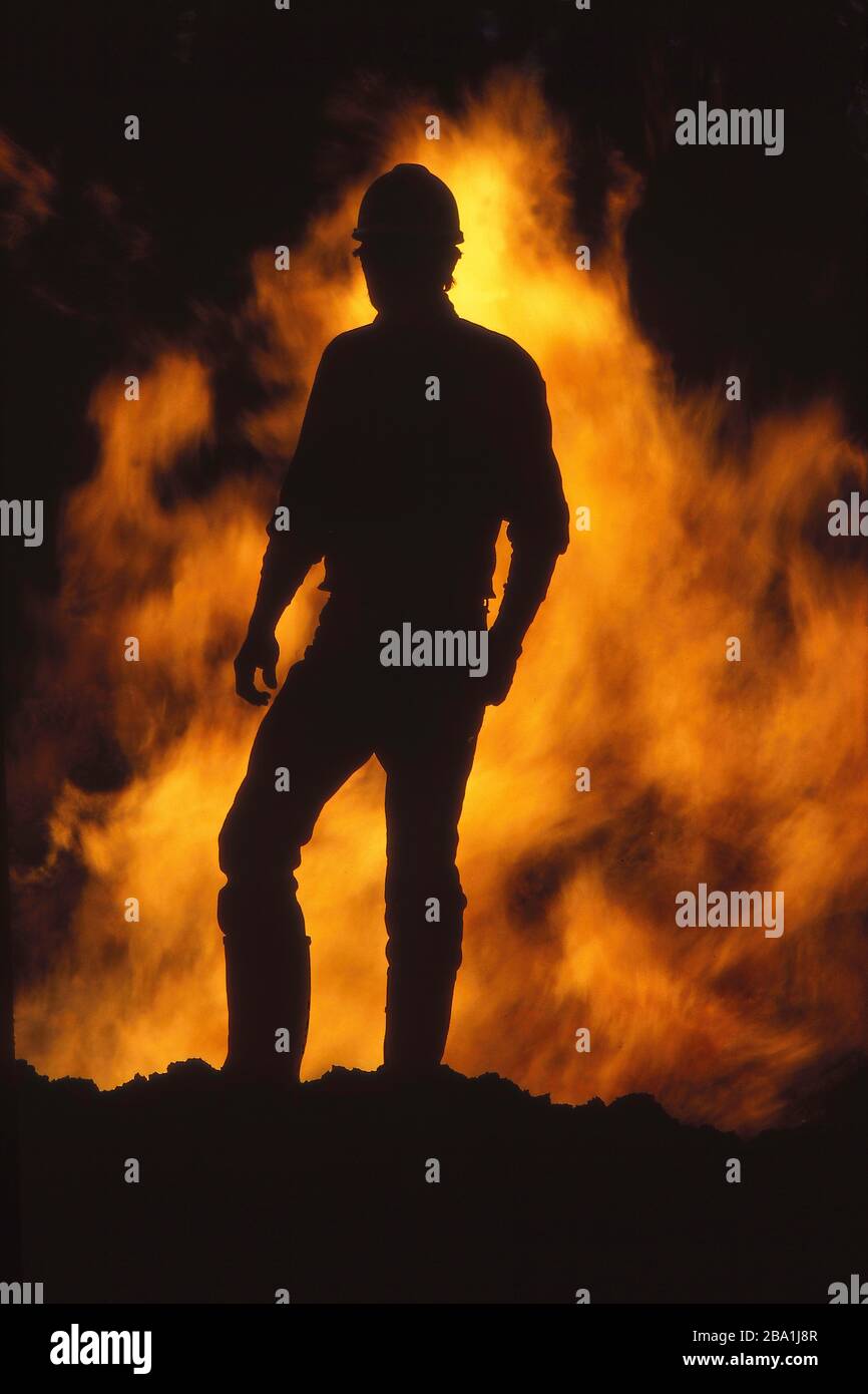Ein Bauarbeiter in einer Hardhat-Silhouette, die von Feuer und Flammen bei einem Unfall auf der Baustelle umrissen wird Stockfoto