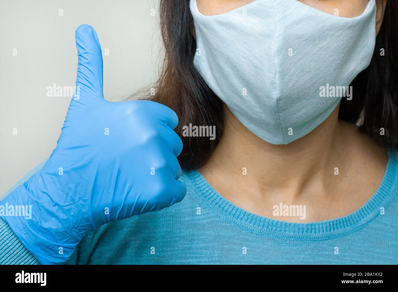 Frau zeigt in blauen Handschuhen und Schutzmaske im Kampf mit Coronavirus, 2019-nCoV, SARS-COV-2, Grippe ok. Konzept der Gesundheitsversorgung und der guten Medizin. Stockfoto