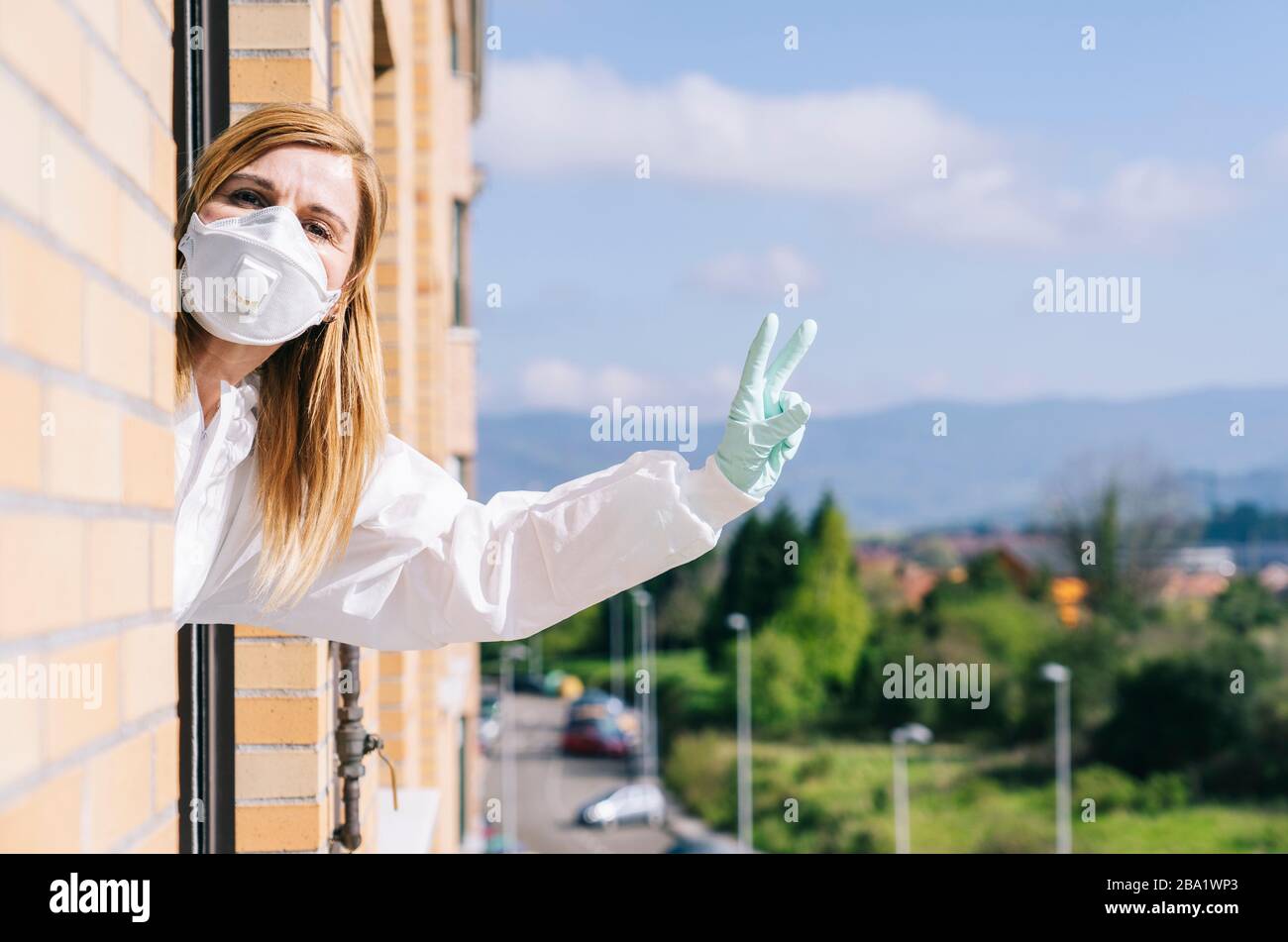 Frau, die aus dem Hausfenster schaut. Sie trägt eine Schutzmaske zur Vorbeugung eines Pandemievirus. Konzeptvirus. Stockfoto