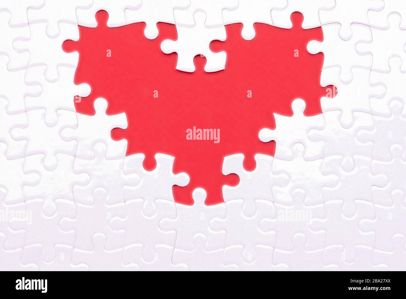 Herz aus weißen Rätseln als Symbol der Liebe auf rotem Hintergrund. Fans mögen Rätsel, die sich ergänzen Stockfoto