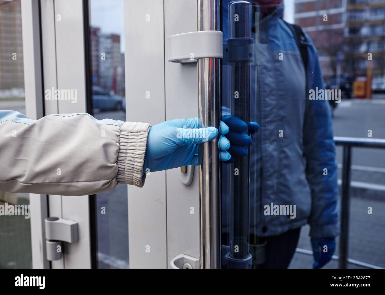 Die Hände der Frau öffnen die Tür mit blauen Handschuhen aus medizinischem Latex, um sich vor Coronavirus zu schützen.Schutz vor Coronavirus und Infektionen. Stockfoto