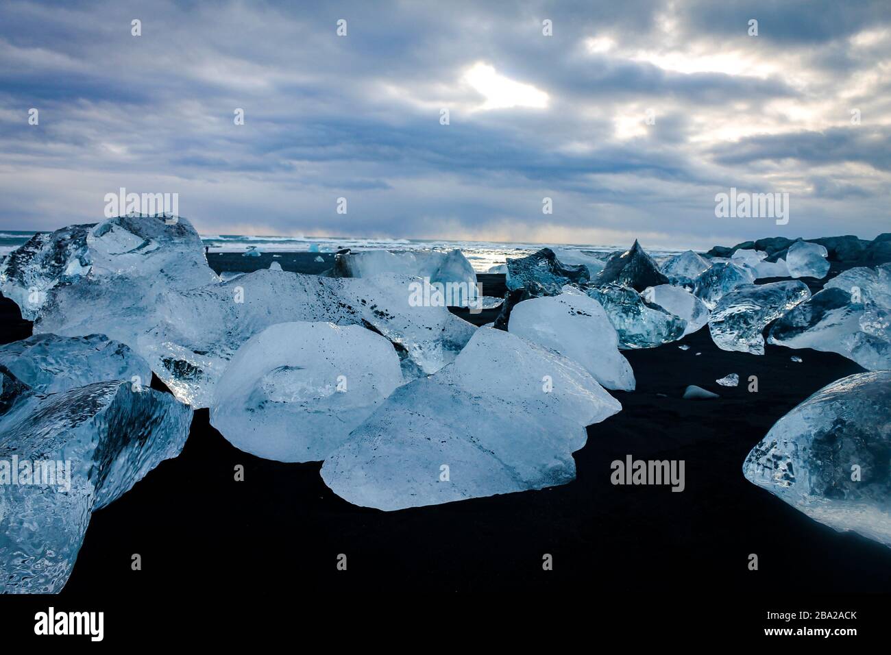 Betuchreiche kleine Eisberge mit verschiedenen Formen machen einen riesigen Kontrast zum schwarzen Sandstrand Stockfoto