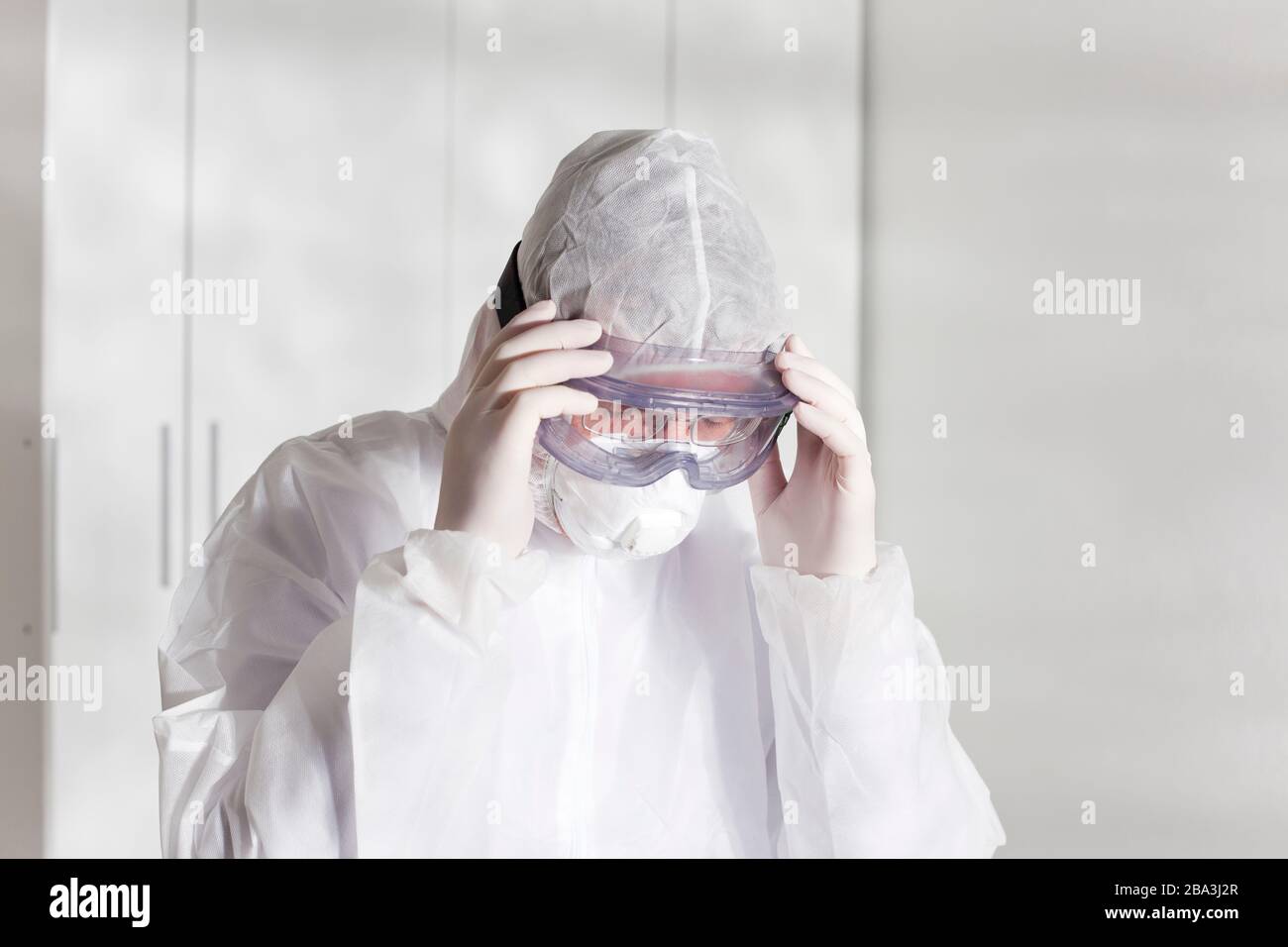 Müder Arzt mit Schutzkleidung wegen Coronavirus in einem Krankenhaus - hellweißer Hintergrund Stockfoto