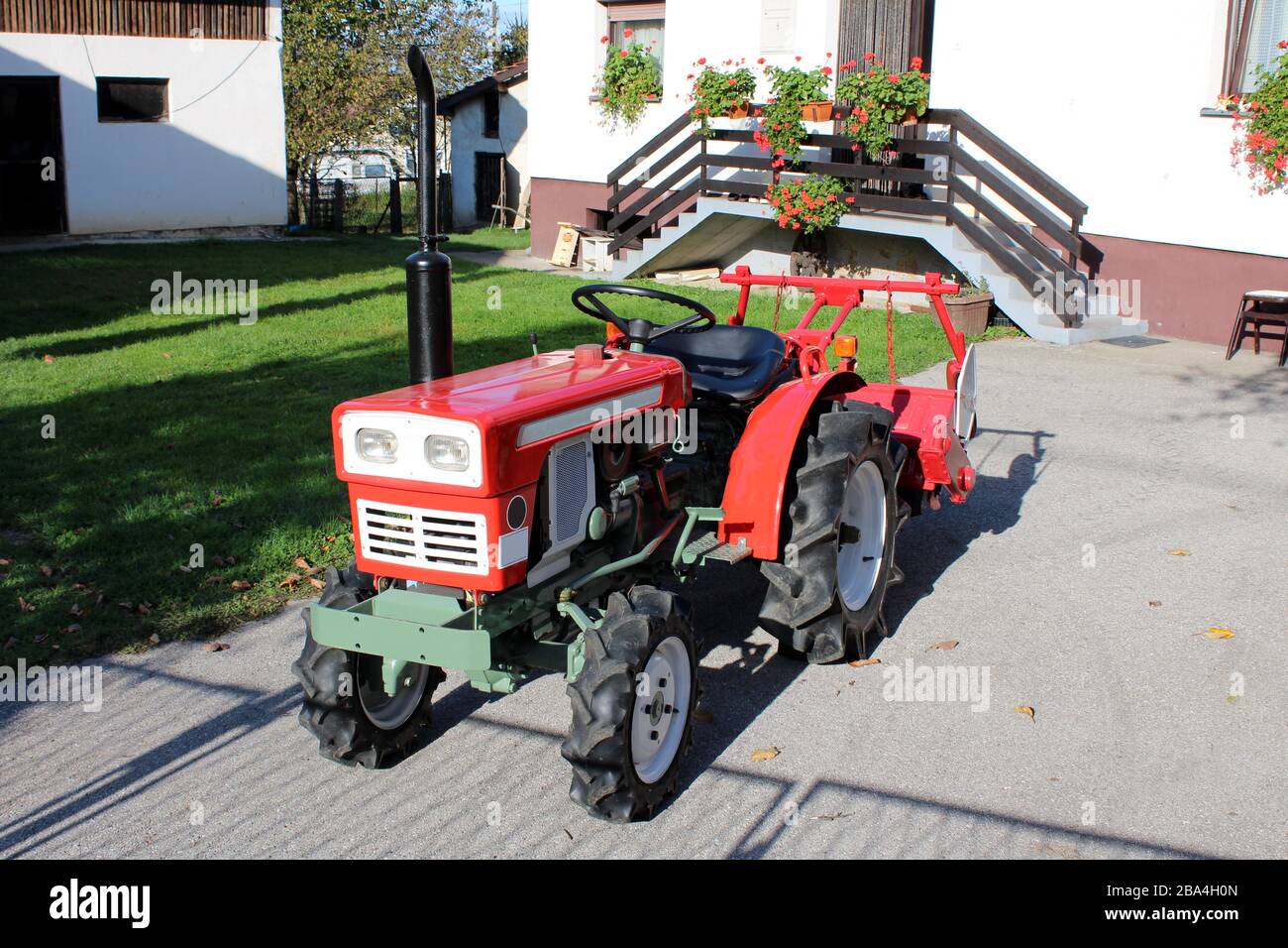 Restaurierter und komplett renovierter alter, retro alter Klein-Kompakttraktor mit neuen Reifen, die auf der gepflasterten Einfahrt des Vorstadt-Familienhauses geparkt sind Stockfoto