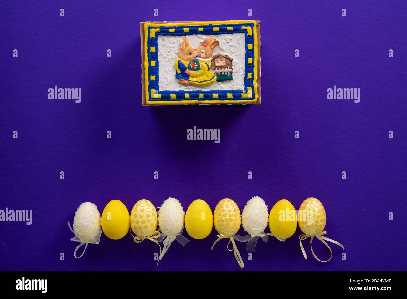 Osterhase und neun gelb-weiße, gefälschte Ostereier aus Kunststoff auf dunkelviolettem Grund Stockfoto