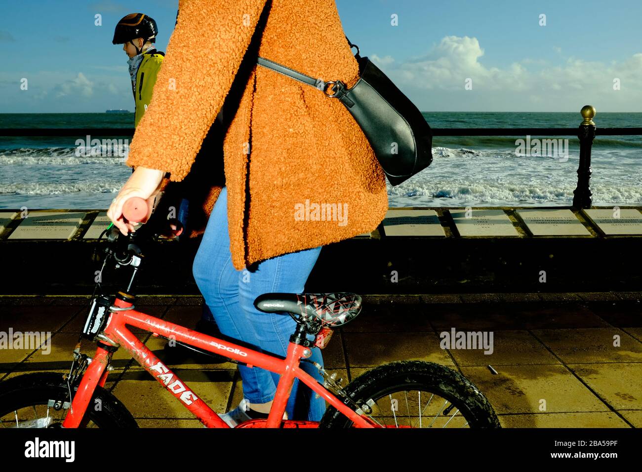 Eine Mama treibt das Fahrrad ihres Sohnes entlang der Strandpromenade Stockfoto