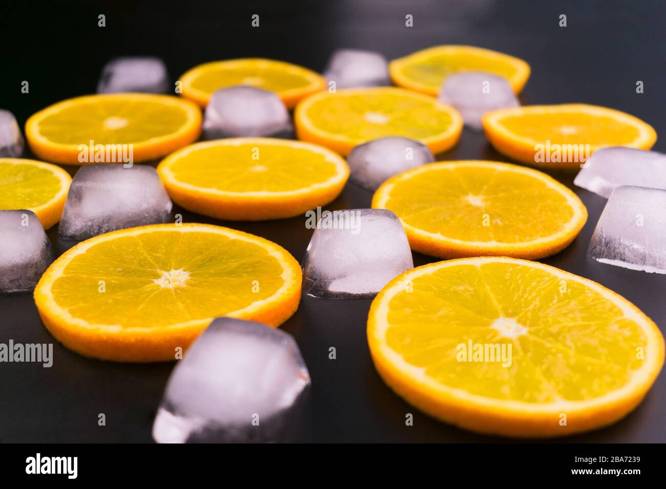 Scheiben von Orange- und Eiswürfeln auf schwarzem Hintergrund. Stockfoto