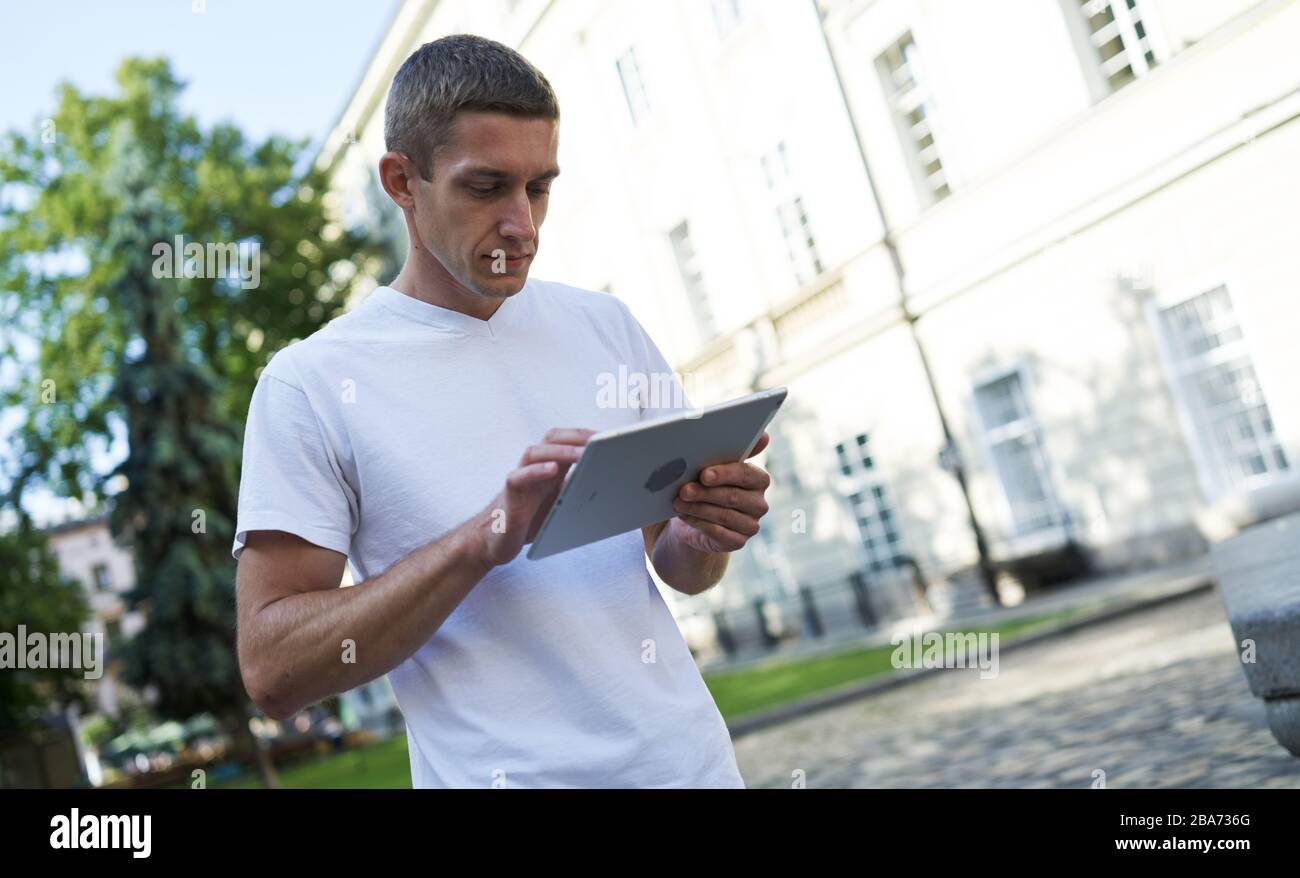 Ein gutaussehender Mann, der auf der Straße steht und etwas auf seinem Tablet sucht Stockfoto