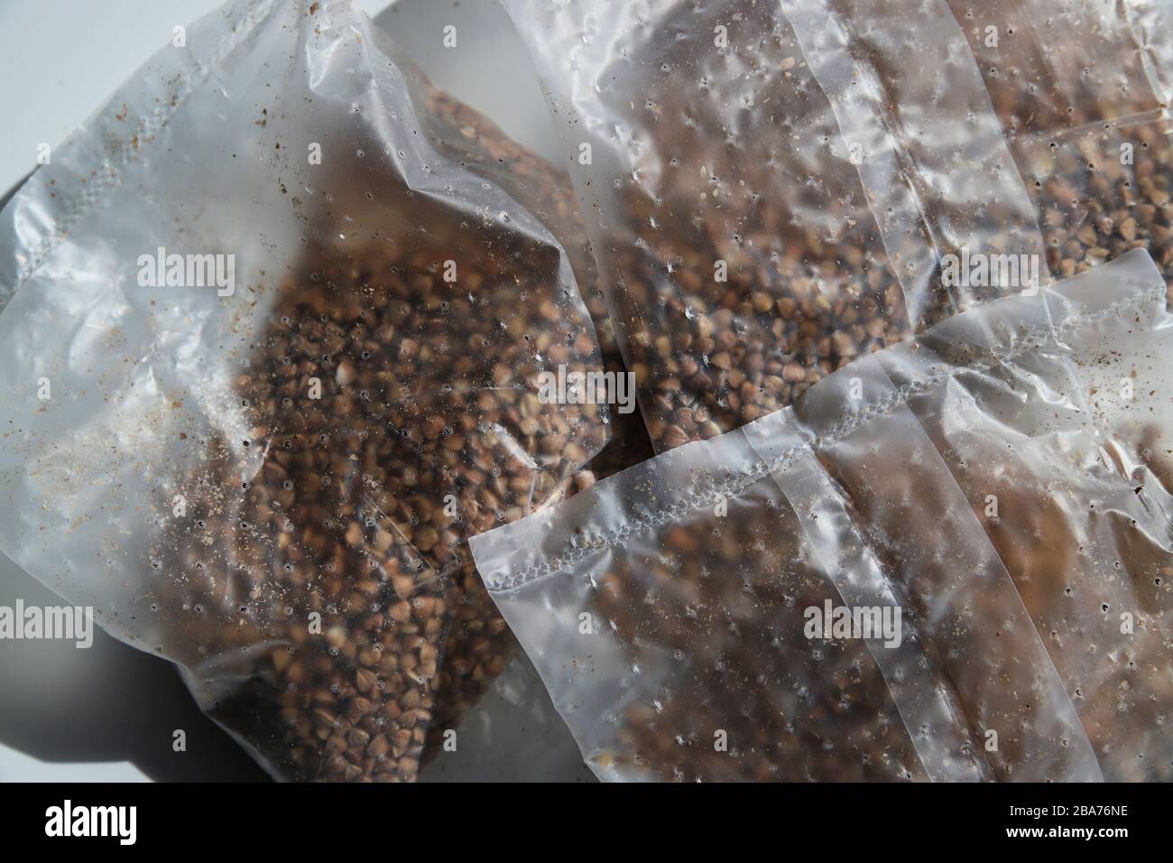 Buchweizen in kochendem Kunststoff-Paket zum Kochen auf weißem Hintergrund am sonnigen Tag. Gesunde Körner zum Mittag- oder Abendessen. Billige Lebensmittel für die Armen in der Krise Stockfoto