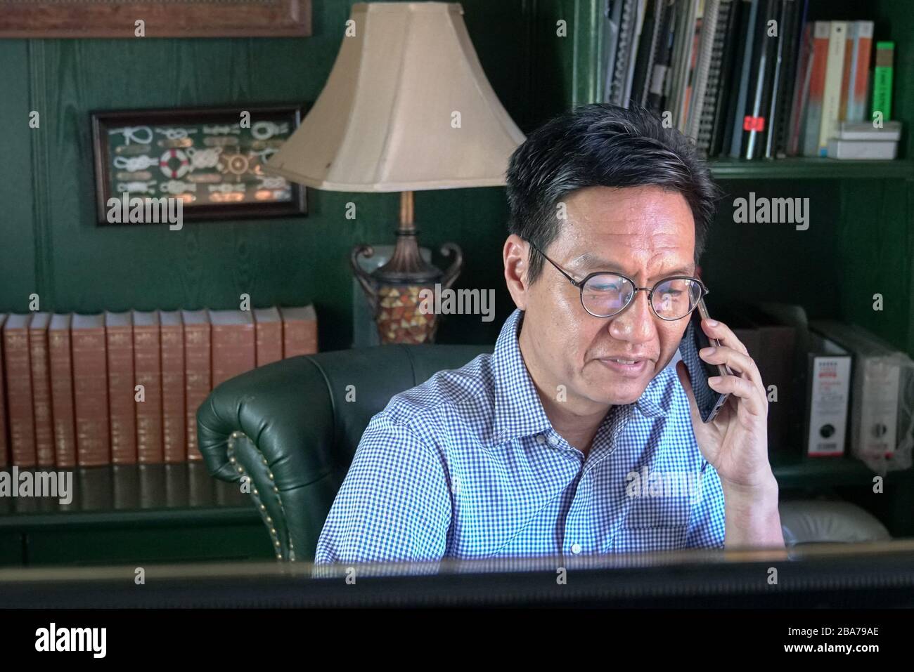 Heimarbeit. Asiatisch-chinesischer Geschäftsmann auf dem Handy in seinem Arbeitszimmer. Stockfoto