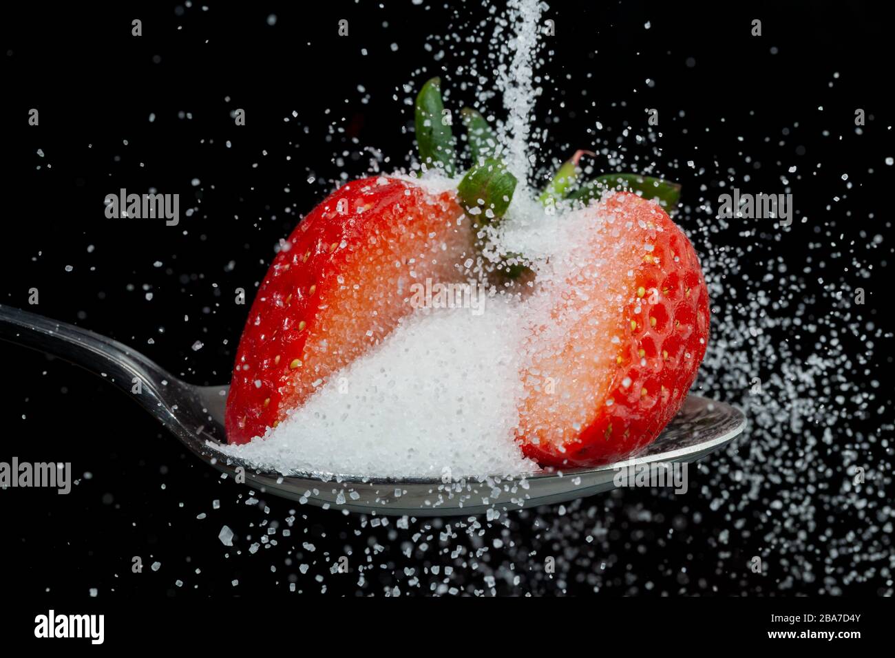 Frische Erdbeere zur Hälfte auf einem Löffel mit einem Haufen herunterfallendem weißem Zucker bestreuen. Konzept des verborgenen Zuckers in Obst Stockfoto