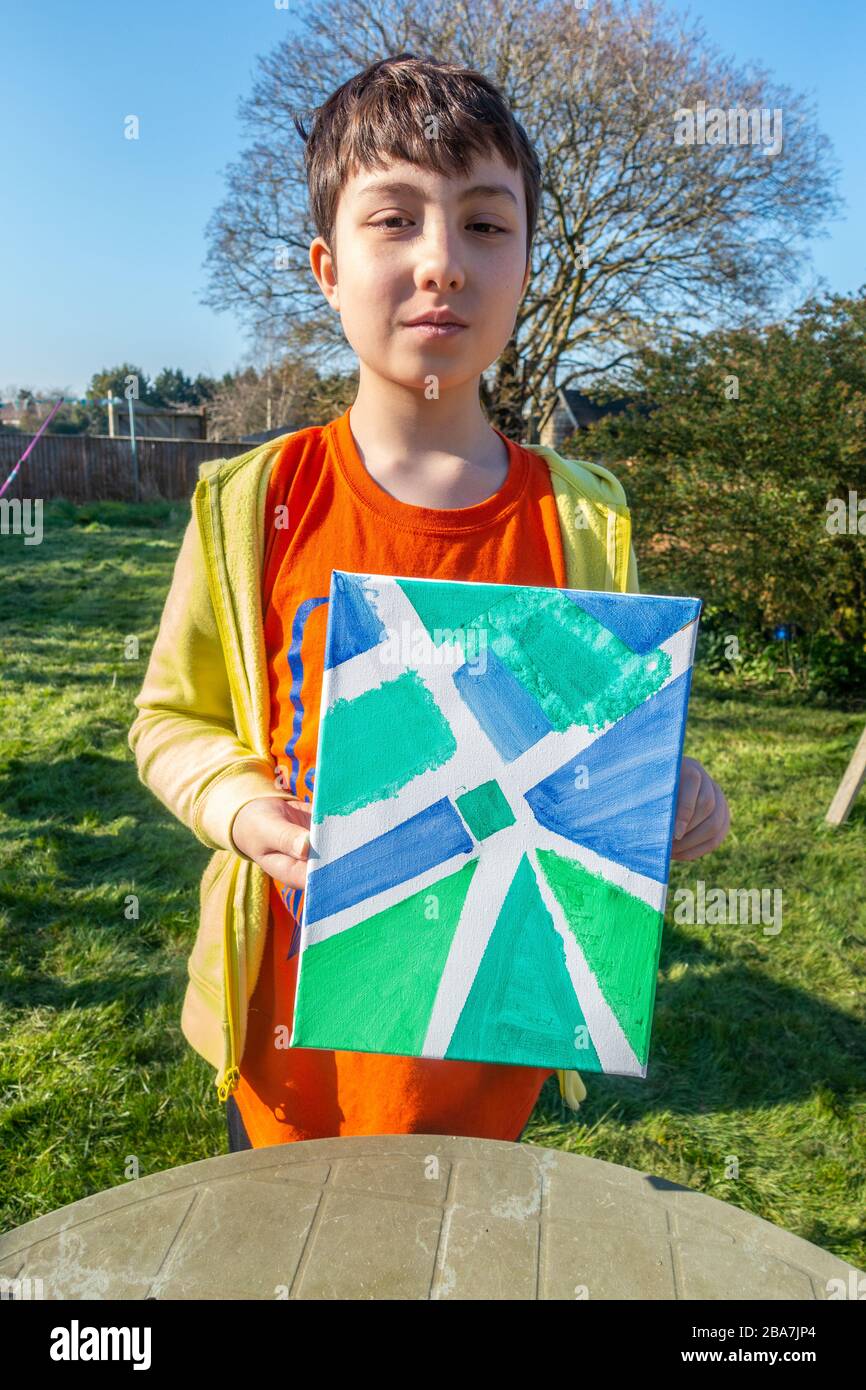 Stolz zeigt ein kleiner Junge das Gemälde aus Acryl auf Leinwand, das er im Garten gemacht hat. Stockfoto