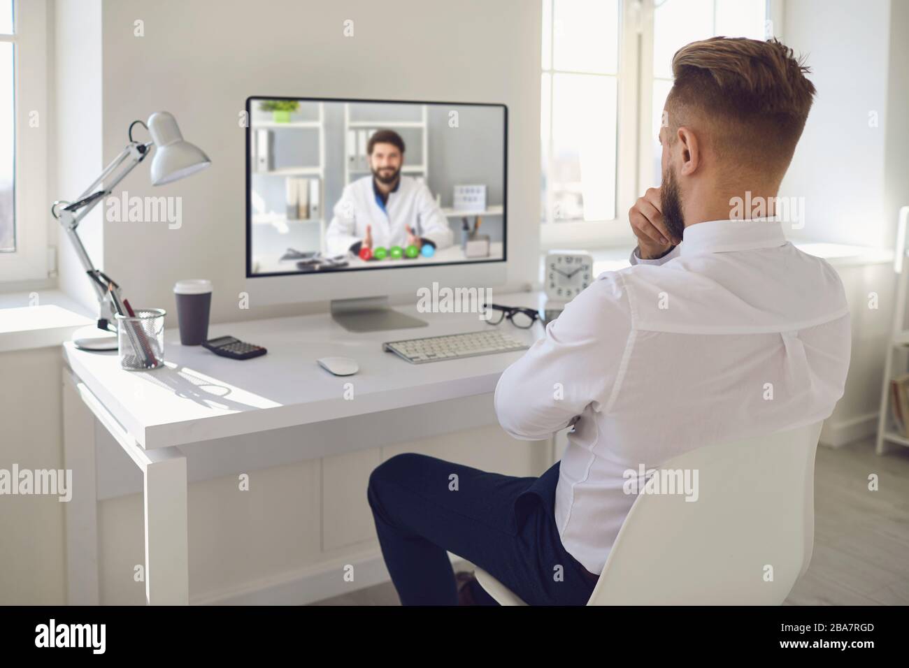 Online-Arzt.EIN Mann, der online mit einem Arzt auf einem Computer an einem Schreibtisch in einem Büro spricht. Medizinische Online-Beratung. Stockfoto