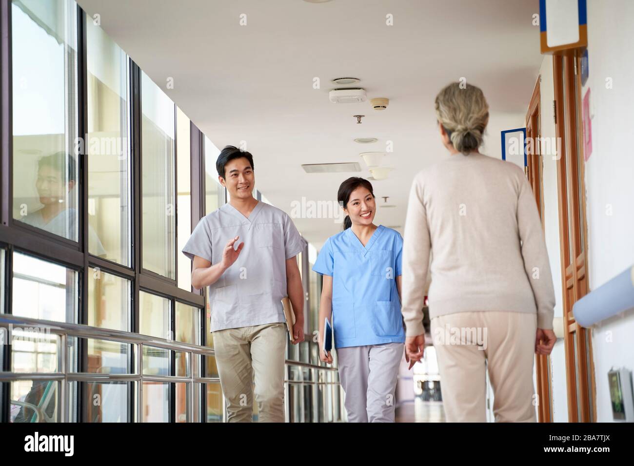 Fröhliche junge asiatische Physiotherapeuten begrüßen die Bewohner im Flur des Pflegeheims Stockfoto