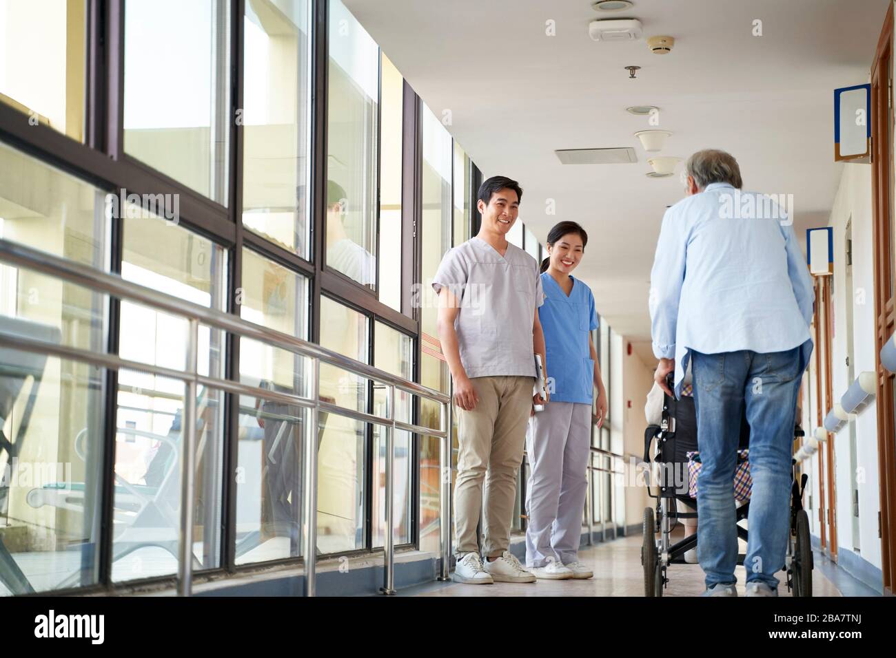 Fröhliche junge asiatische Physiotherapeuten begrüßen die Bewohner im Flur des Pflegeheims Stockfoto