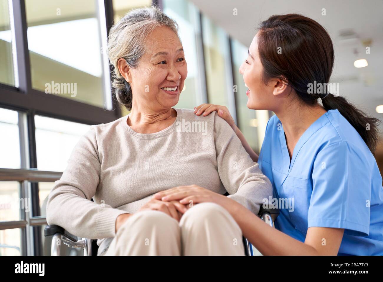 Freundliche Pflegekraft im Pflegeheim, die mit der asiatischen Seniorin im Flur spricht Stockfoto