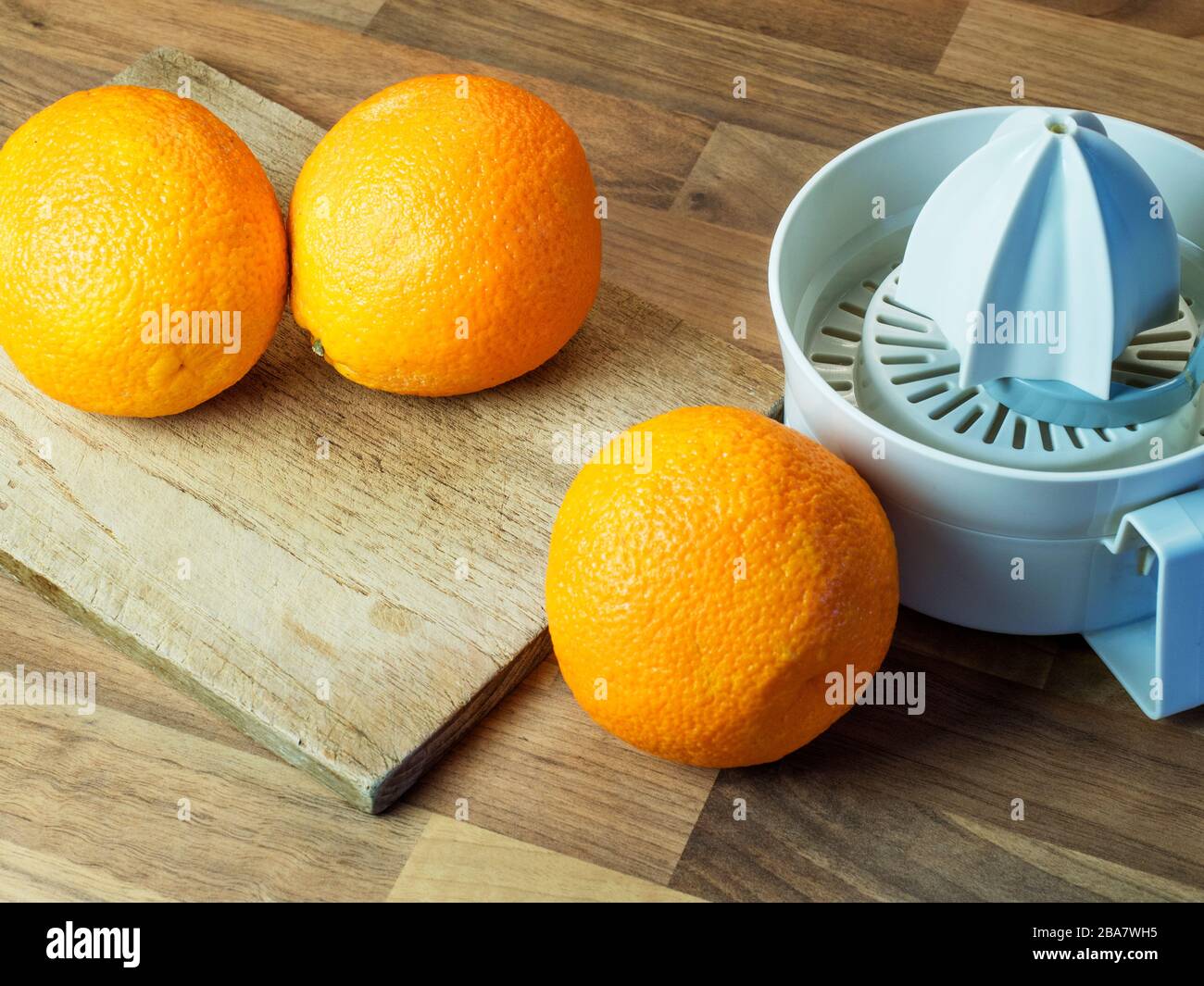 Drei Orangen mit einem Hackbrett und einer orangefarbenen Presse auf einer Arbeitsfläche der Holzblockküche Stockfoto