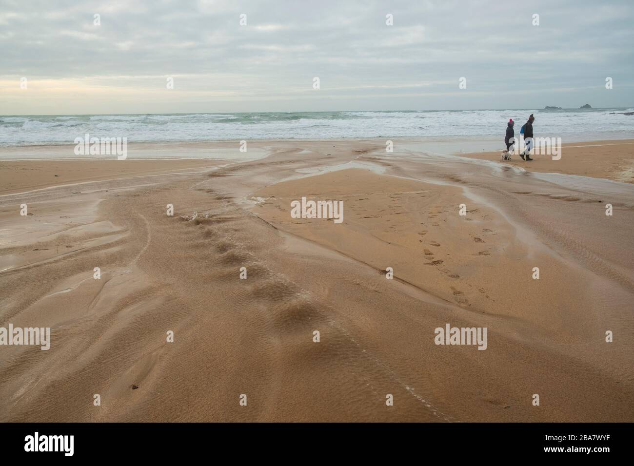 Constantine Bay, ein schöner Sandstrand in der Nähe von Ttevose in Cornwall, an einem herbstlichen Tag mit zwei Leuten, die die frische Luft genießen, die mit einem kleinen Hund spazieren geht Stockfoto