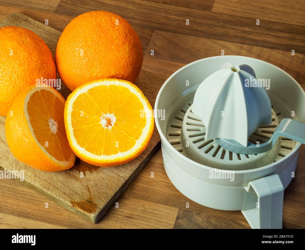 Orangen und eine halbierte Orange mit einem Hackbrett und einem orangefarbenen Quetschaufsatz auf einer Arbeitsfläche der Holzblockküche Stockfoto