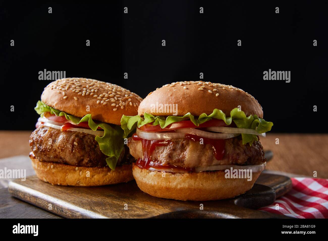 Zwei Burger auf Holzschneidplatten isoliert auf Schwarz Stockfoto