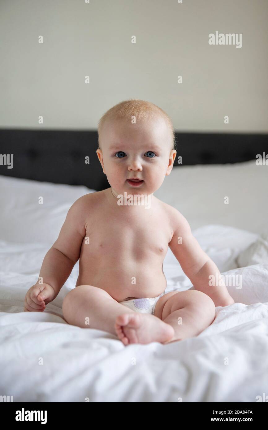 Süßes Baby, das eine Windel trägt, saß auf einem Bett, das auf die Kamera blickt Stockfoto