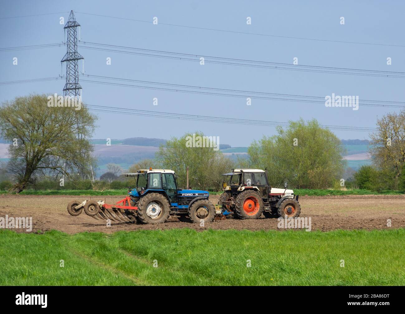 Beilby, East Yorkshire, 21.04.2018 - EIN blauer Ford-Traktor und ein weißer CASE-Traktor pflügen zusammen ein Fiel. Stockfoto