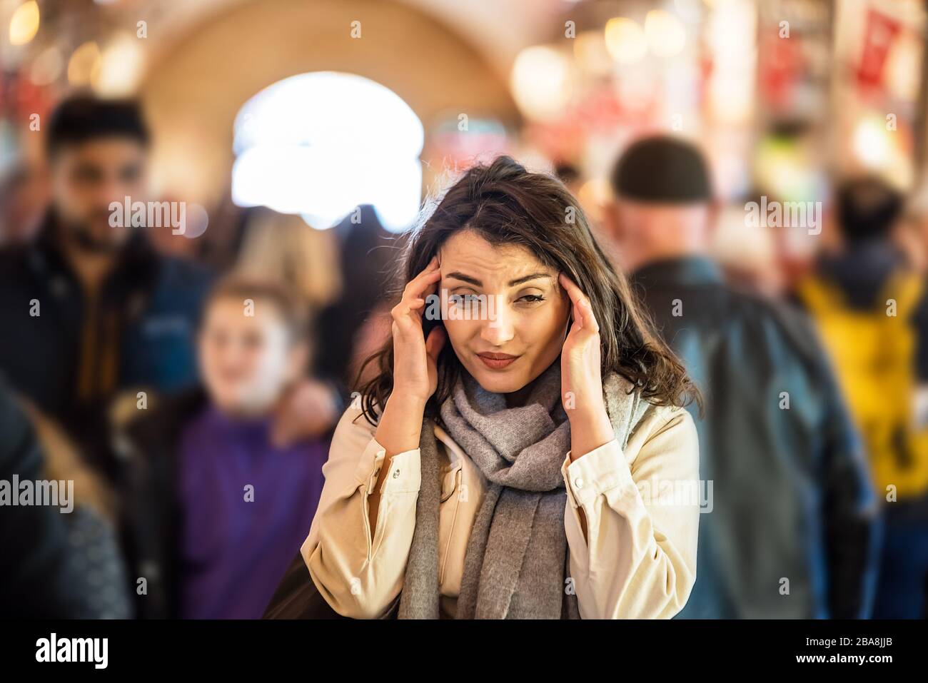 Schöne Frau in modischer moderner Kleidung leidet unter Migräne- oder Kopfschmerzproblemen, während sie die Menschenmenge auf der Straße steht. Stockfoto