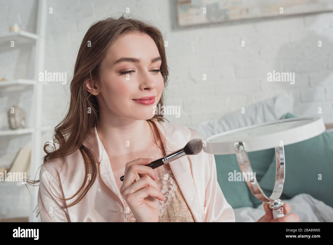 Selektive Fokussierung blonder Mädchen mit Kosmetikbürste und Spiegel im Zimmer Stockfoto