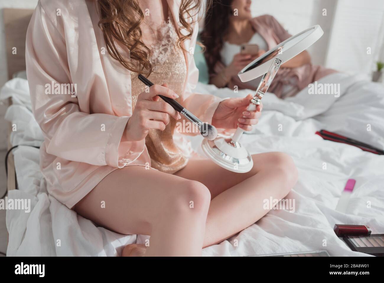 Beschnittener Blick auf blonde Mädchen, die auf der Junggesellenparty Kosmetikbürste und Spiegel mit Freund im Zimmer hält Stockfoto