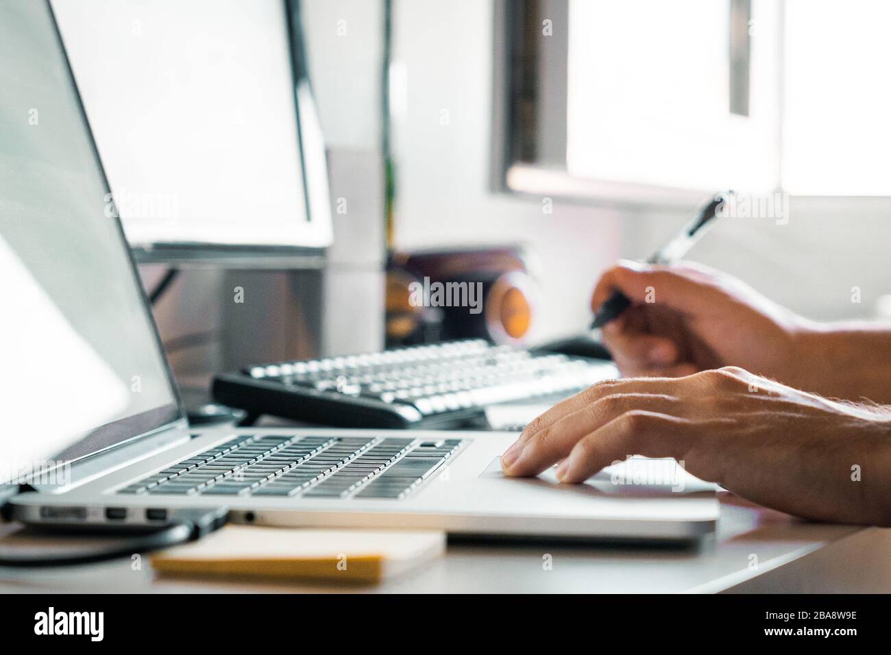 Person, die einen Stift mit Computern von zu Hause aus am Schreibtisch hält Stockfoto
