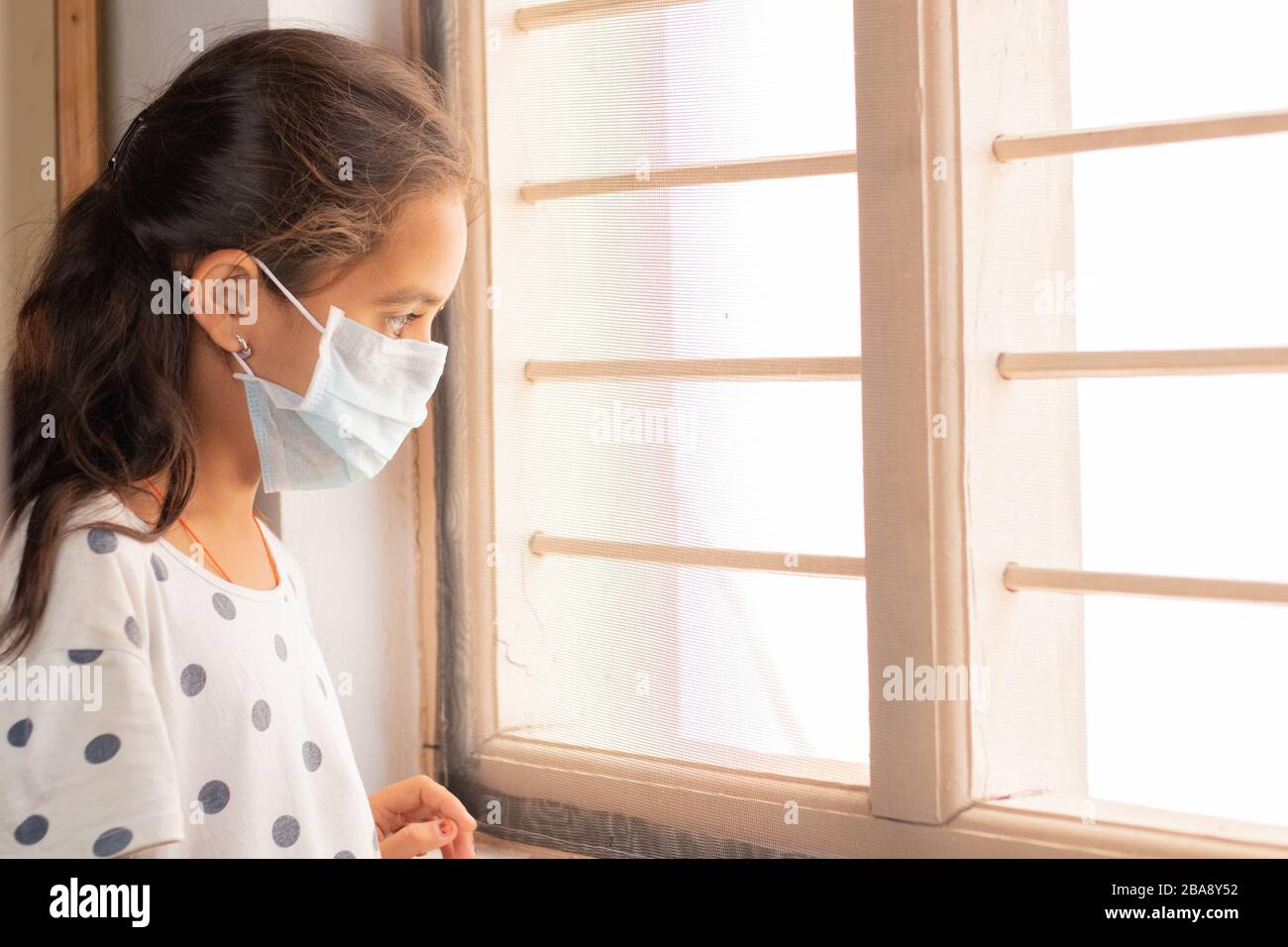 Trauriges junges Mädchen, das während der häuslichen Isolation durch das Fenster schaut und dabei beobachtet - Coronavirus oder Covid-19 Quarantänekonzept. Stockfoto