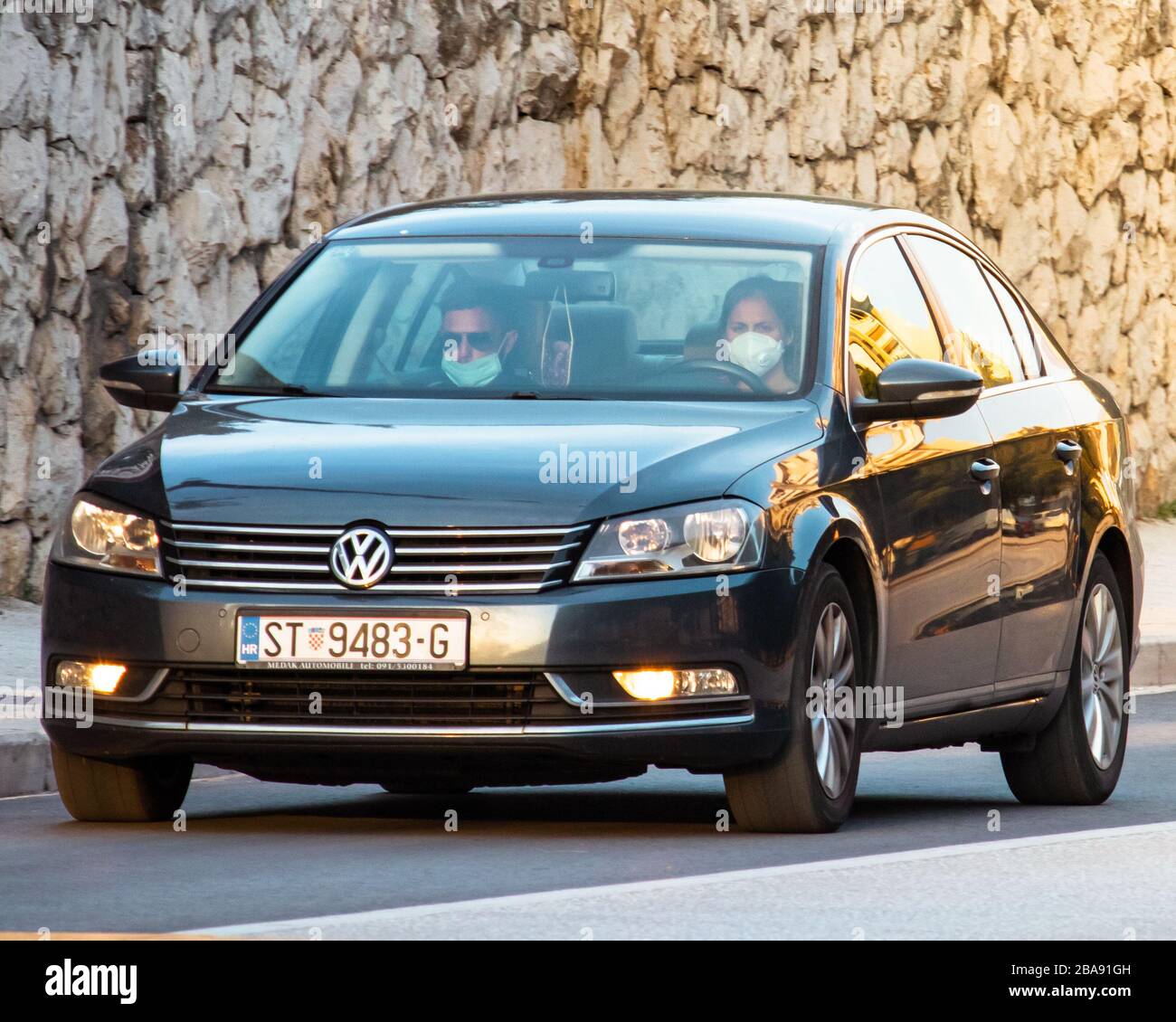 Ein Paar fährt einen schwarzen volkswagen, der beim Ausbruch des Corona-Virus Gesichtsmasken trägt. Pendeln zur Arbeit Stockfoto