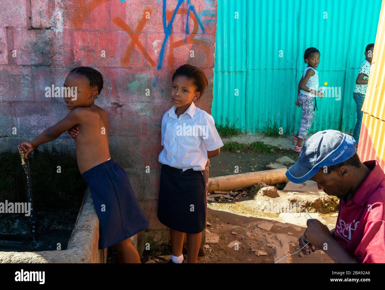 Kinder, die in der Imizamo Yethu Township leben, stehen am öffentlichen Wasserhahn, der Hout Bay, Kapstadt, Südafrika Stockfoto