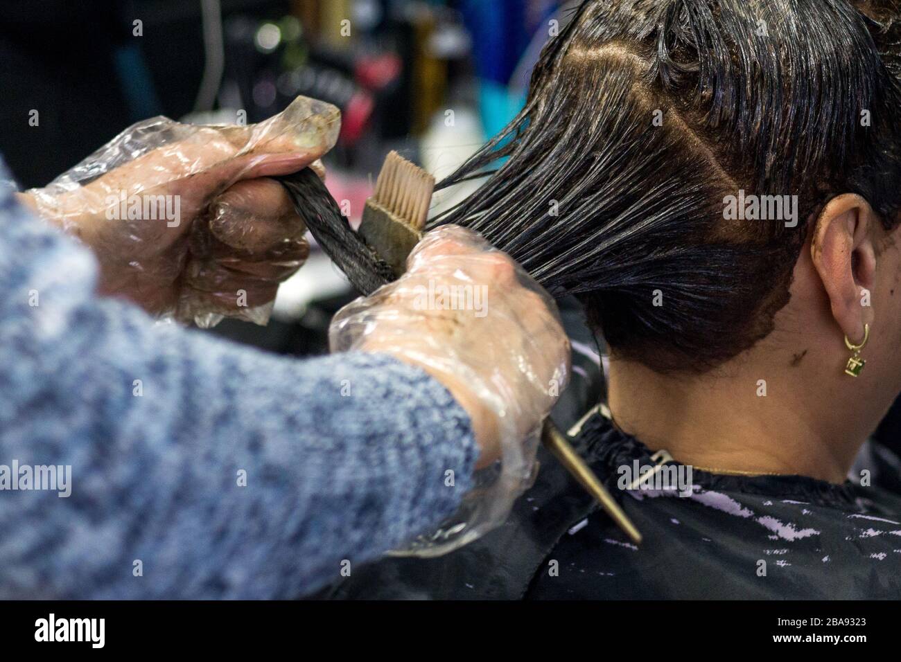 Attraktive Brünette gründlich färben Haare der weiblichen Klienten, während sie im Stuhl sitzt im Beauty Salon Friseur Stockfoto