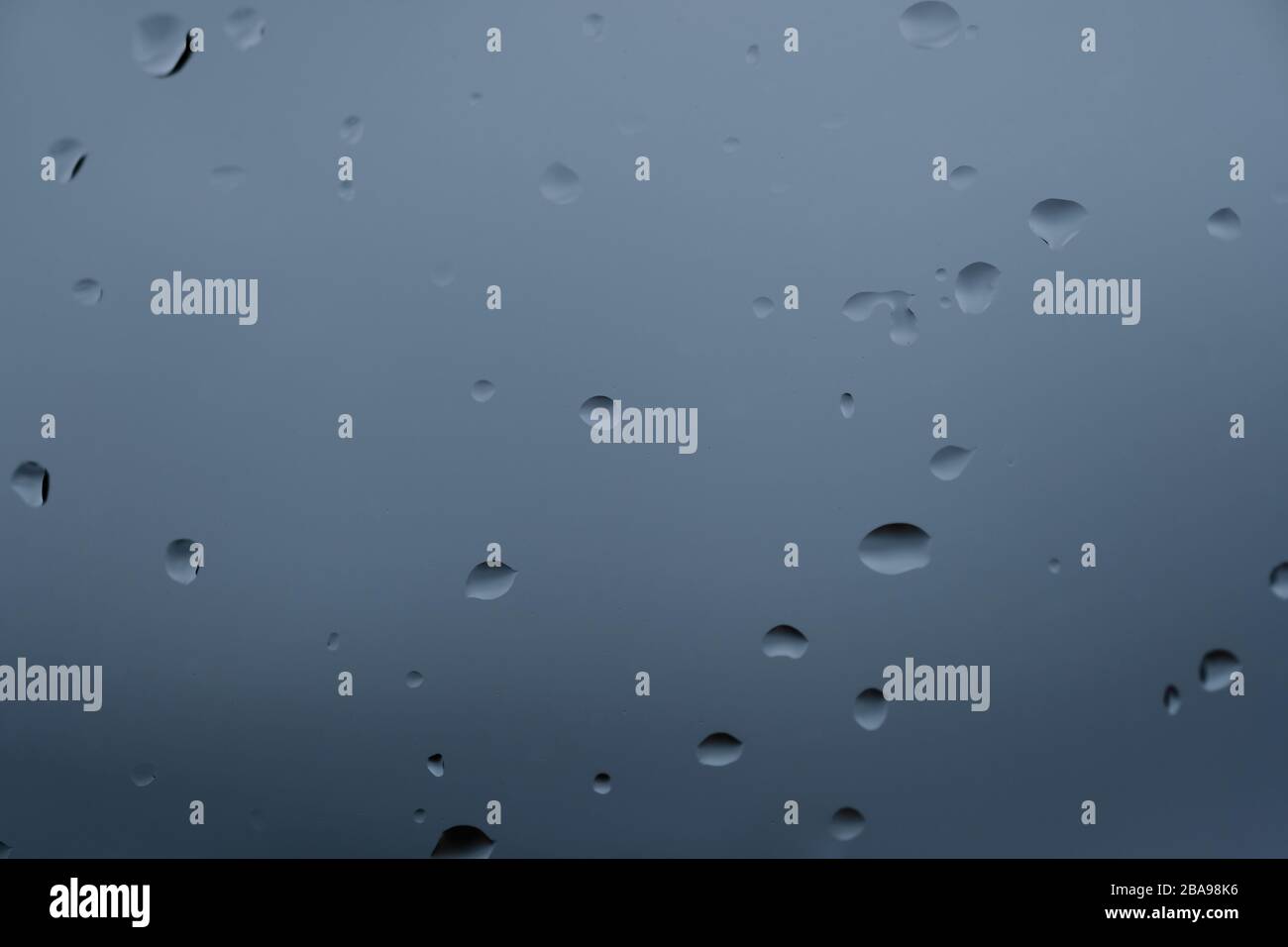 Regenwasser fällt auf Glas über verschwommenen blauen Hintergrund, abstraktes Texturmuster Stockfoto