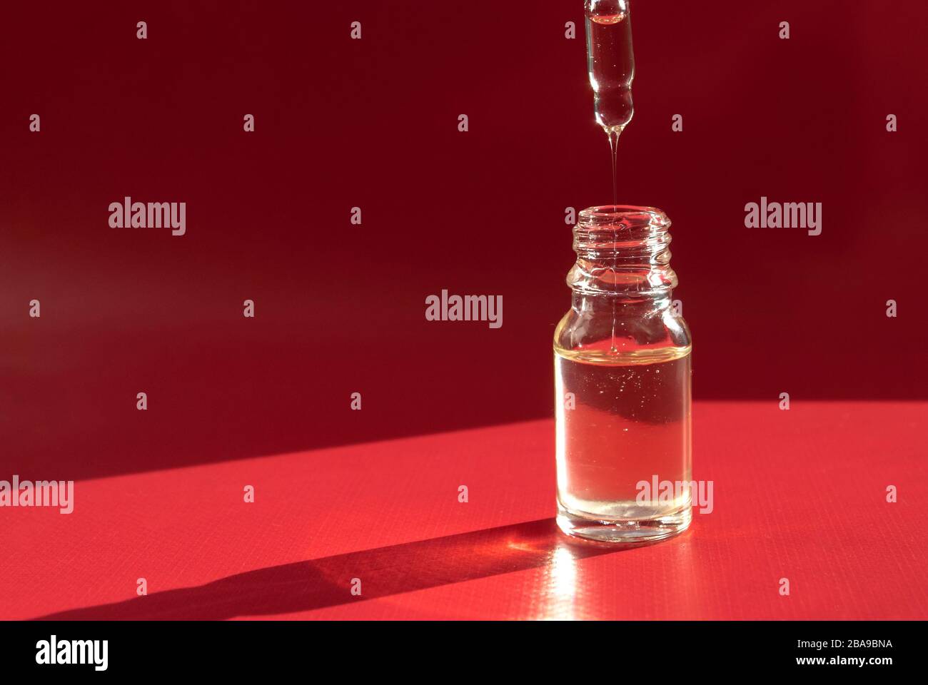 Kosmetik in einer transparenten Flasche mit einem Tropfer auf rotem Hintergrund. Harte Schatten. Platz für Text Stockfoto
