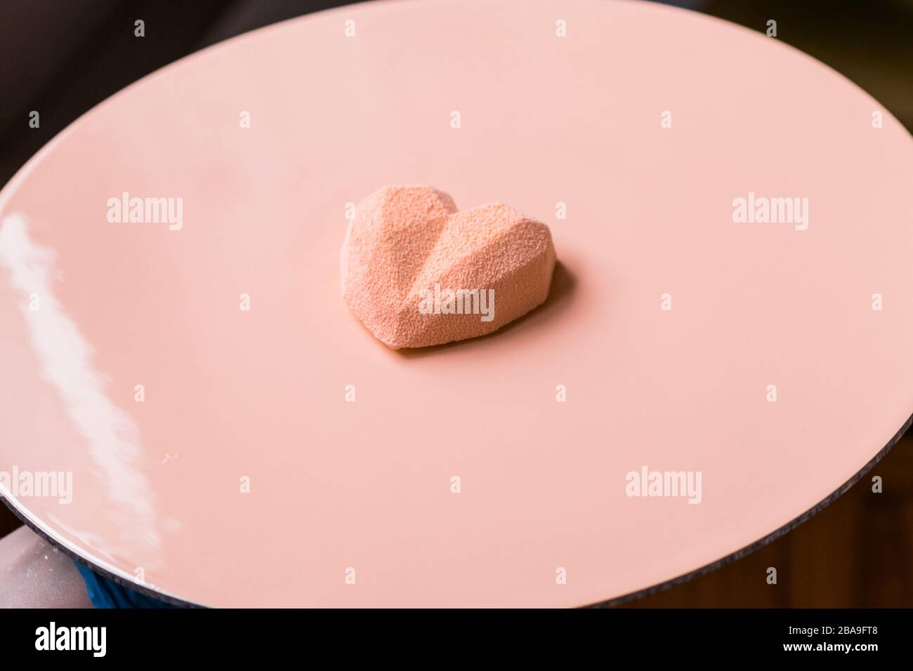 Nahaufnahme des Konditors schmückt den Kuchen mit Veloursleder mit der Spritzpistole. Modernes französisches Mousse Gebäck Dessert mit Schokoladenvelour. Herzform Stockfoto