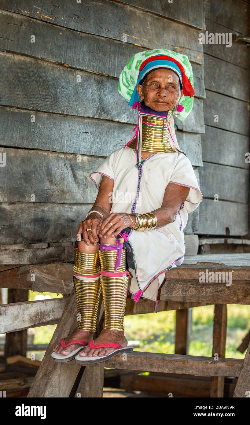 Die alte Padaung-Frau im traditionellen Kleid und mit Metallringen um Hals, Arme und Beine sitzt auf einer Treppe in einem Dorfhaus. Stockfoto
