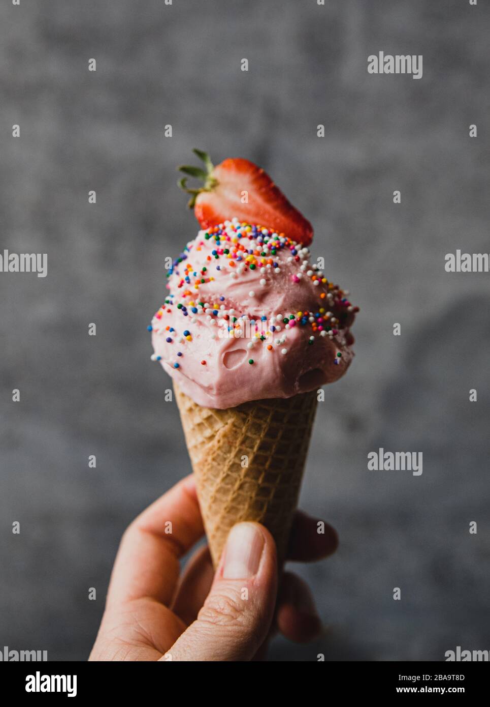 Hand hält Erdbeer Eis-Kegel vor grauem Hintergrund. Stockfoto