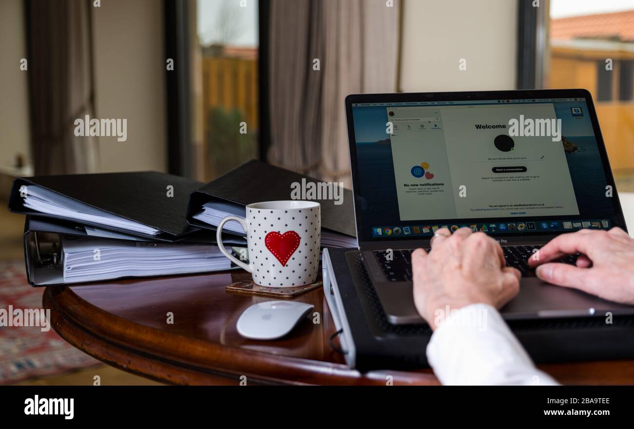 Frau, die zu Hause auf einem Laptop auf dem Tisch arbeitet, auf dem der Bildschirm die Skype-Anwendung zeigt Stockfoto