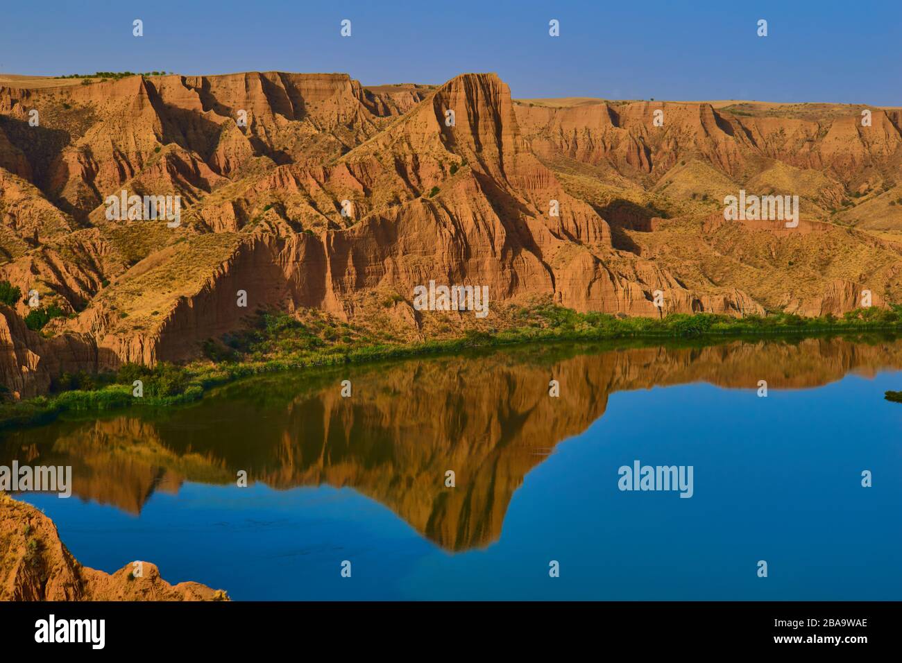 Schöne Landschaft mit roten Felsen und See im Vordergrund mit Reflexion im Wasser der Berge mit klarem Himmel auf den Barrancas de Burujon Stockfoto