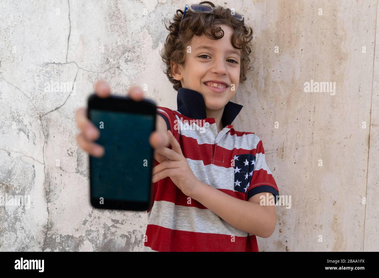 Schuljunge, die Smartphone-Bildschirm draußen vor einem texturierten Hintergrund aus Betonwand zeigen Stockfoto