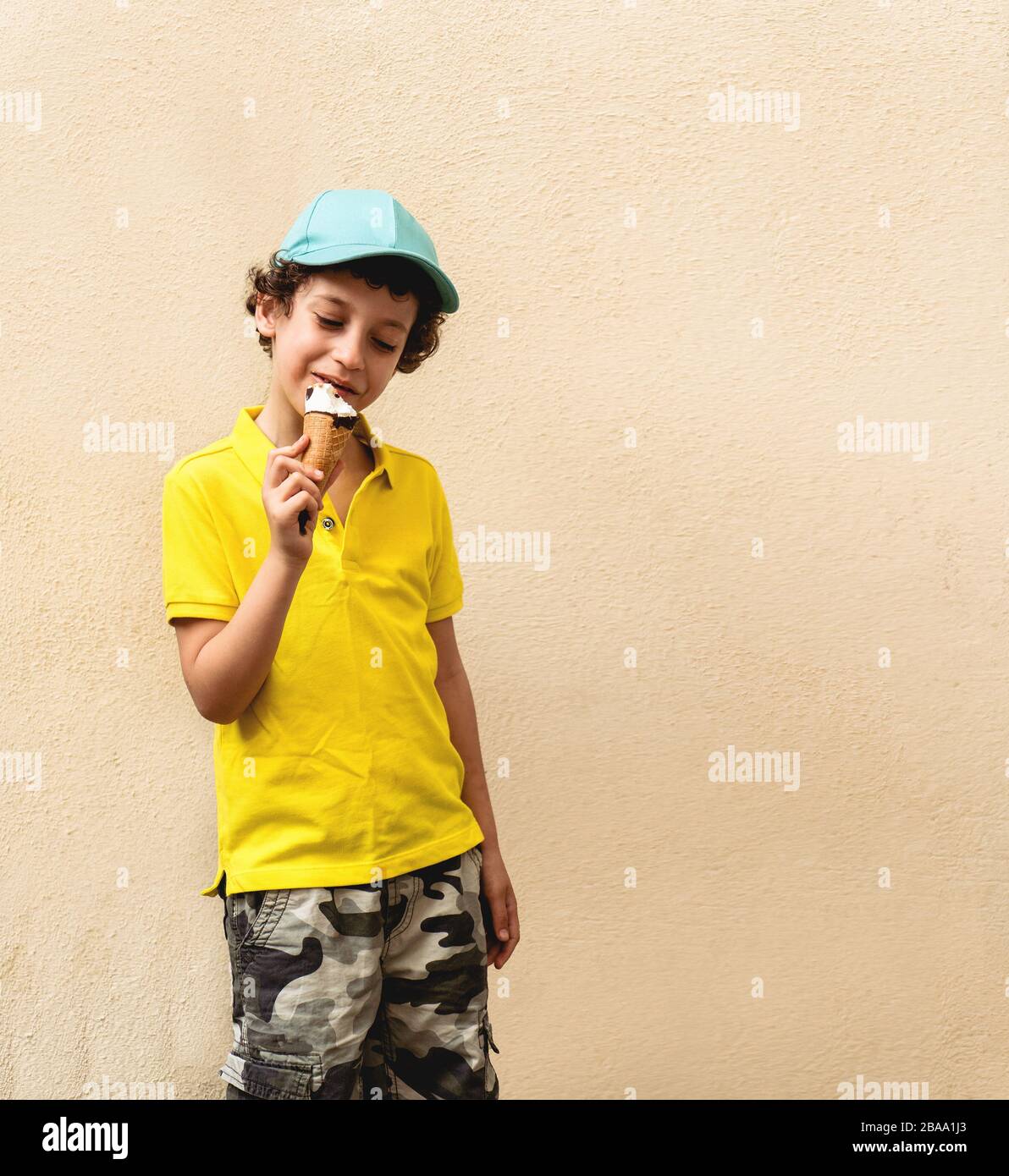 Junge 7 Jahre alt Kerl essen ein Eis im Freien gegen eine Betonwand. Stockfoto