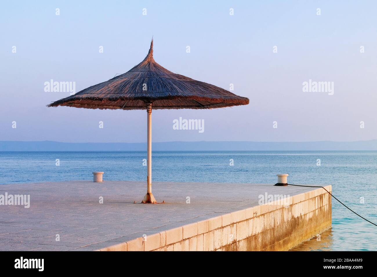 Strohschirm im tropischen idyllischen Resort. Blaues Meer und Himmel mit hellgelbem Sonnenlicht bei Sonnenuntergang. Happy Vacations Konzept. Stockfoto