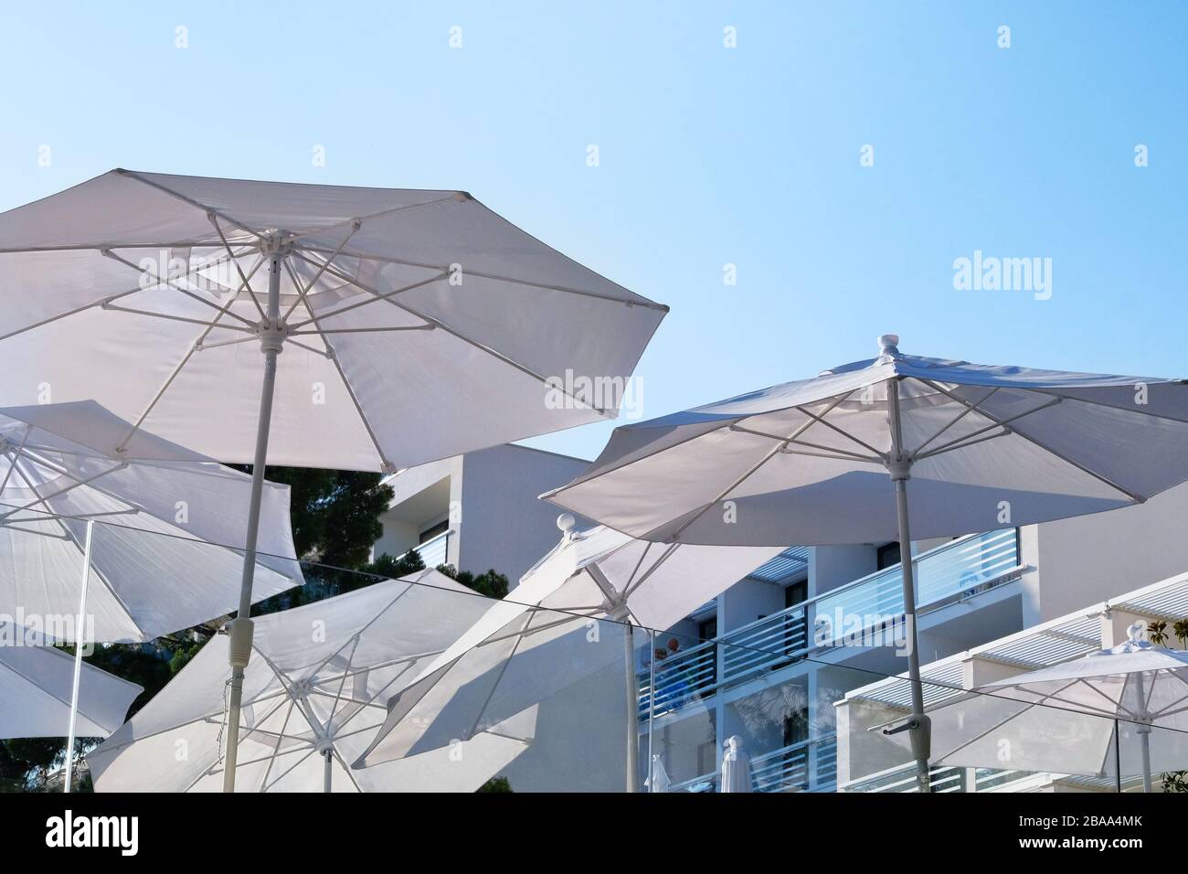 Weiße Sonnenschirme, Sonnenschirme und Sonnenschirme für Entspannung und Komfort auf der Terrasse des Hotels an der Küste. Fröhlicher Sommerurlaub und Resortkonzept. Stockfoto